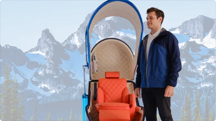 A man stands beside the Apex hyperbaric oxygen therapy (HBOT) chamber, which is open to show its red cushioned chair and an arched blue frame. The man and the chamber are set against a backdrop of snowy mountain peaks.