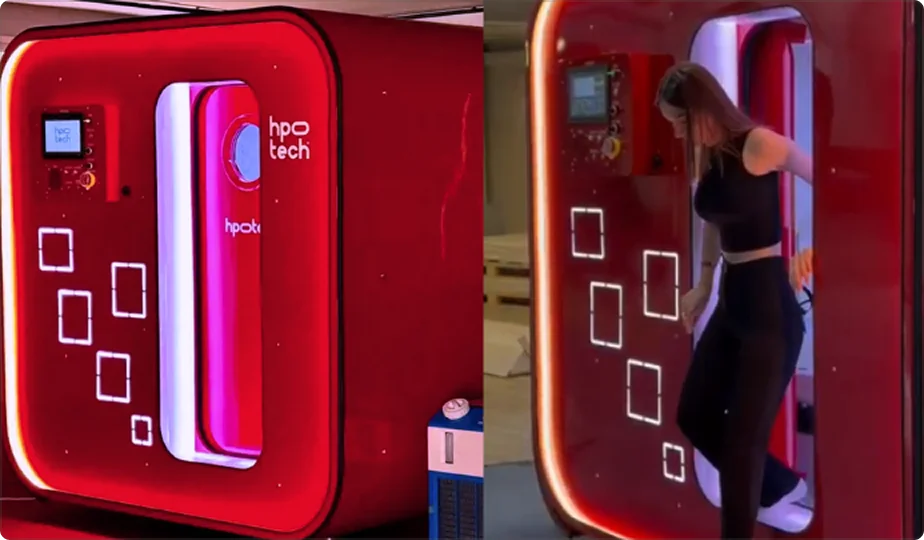 A large red Matrix hyperbaric oxygen therapy (HBOT) chamber with digital controls; on the right, a woman in black athletic wear is stepping out of the chamber through its illuminated entrance.