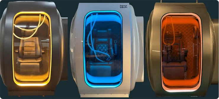 Three images of the interior of the Zeugma hyperbaric oxygen therapy (HBOT) chamber and glowing windows; yellow on the left, blue in the center, and orange on the right, each containing a comfortable recliner chair inside.